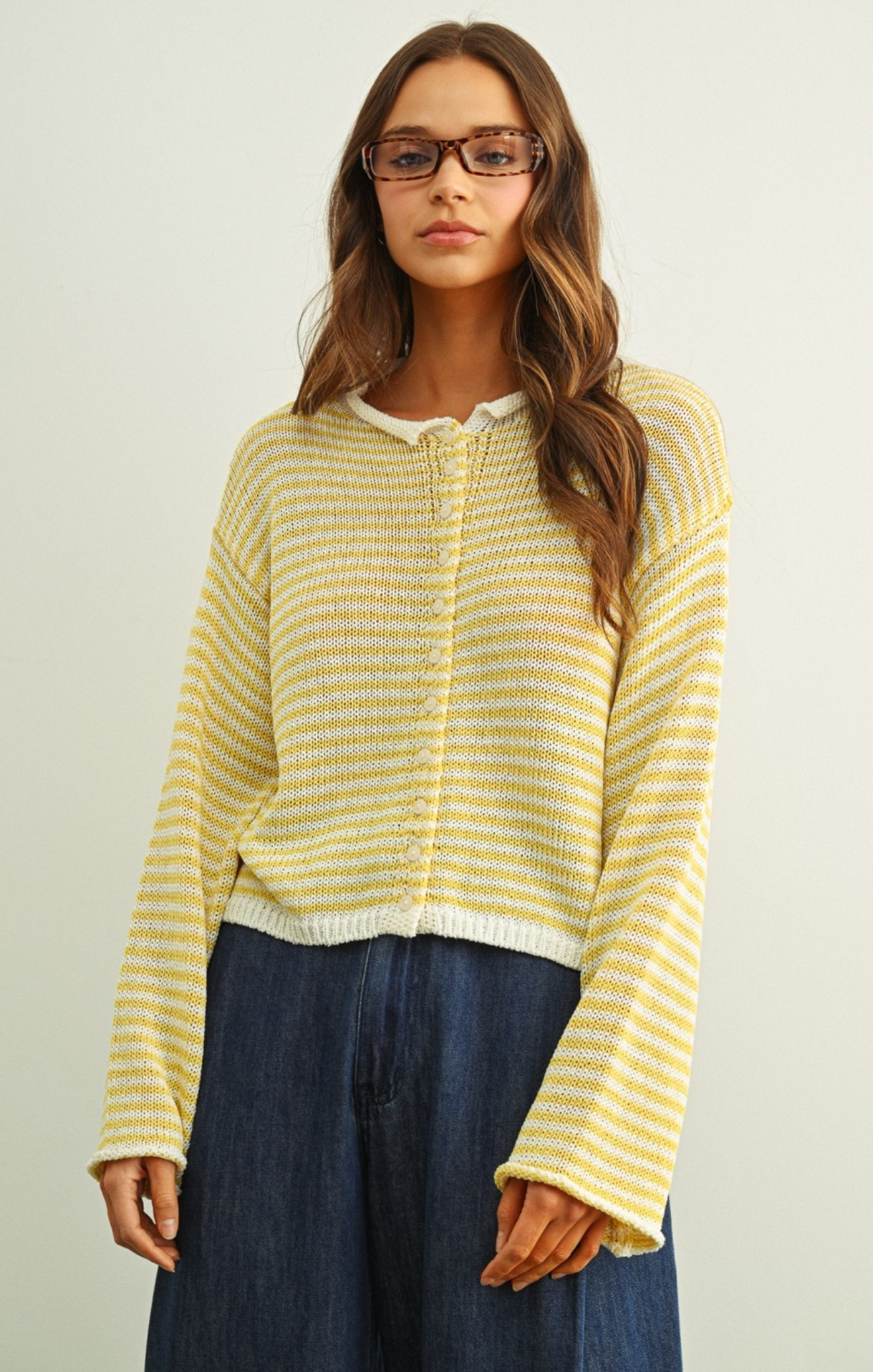 Woman wearing a yellow striped sweater and blue pants against a plain background