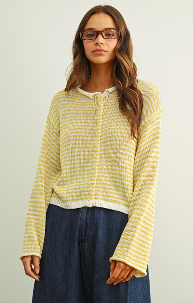 Woman wearing a yellow striped sweater and blue pants against a plain background