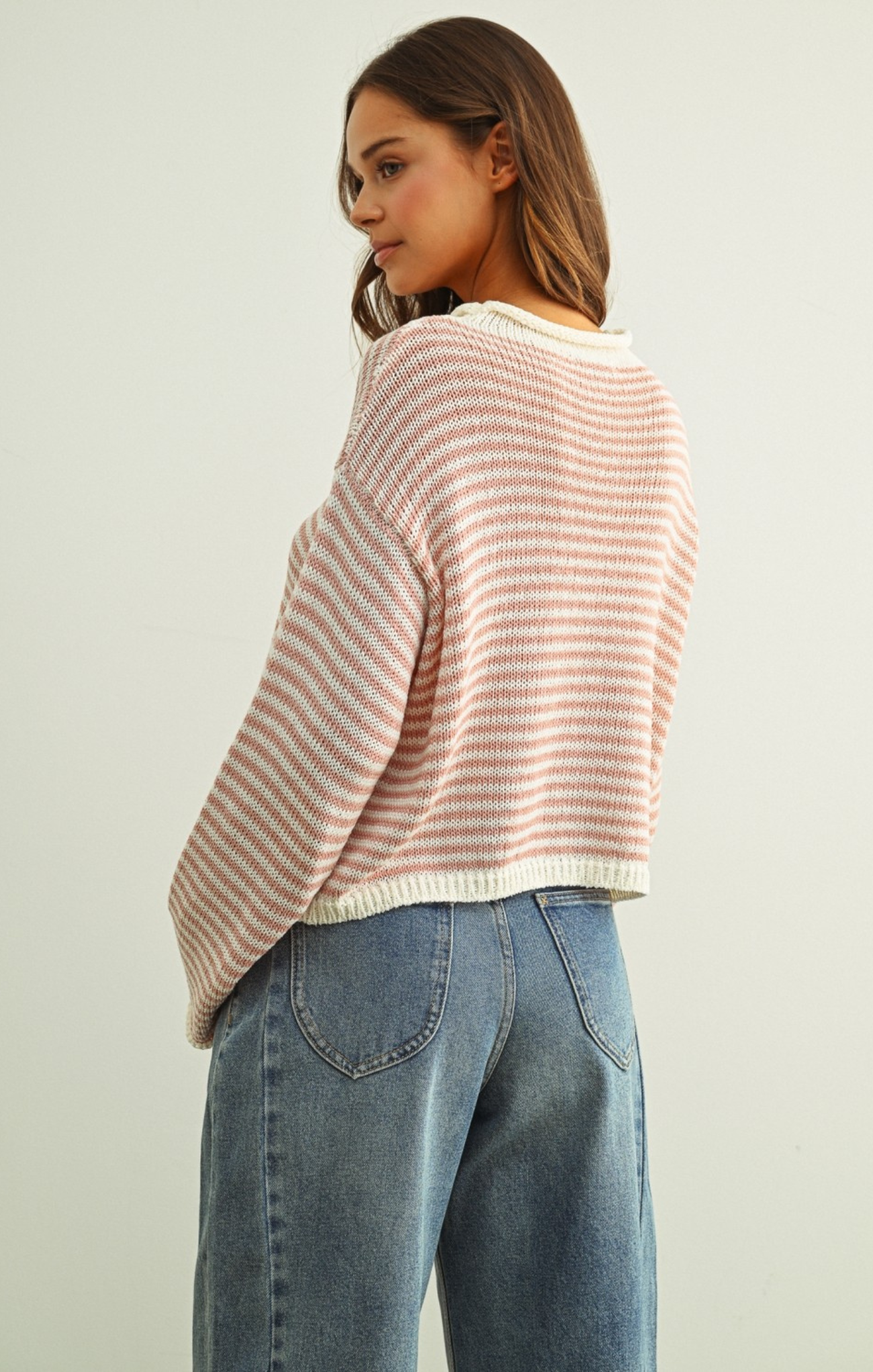 Woman wearing a striped sweater and jeans against a plain background