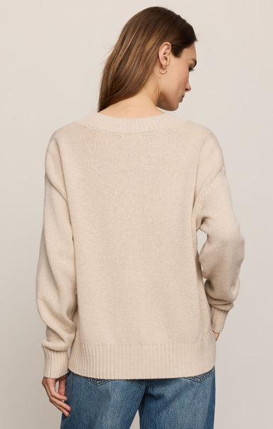 Woman wearing a beige sweater and blue jeans against a plain background