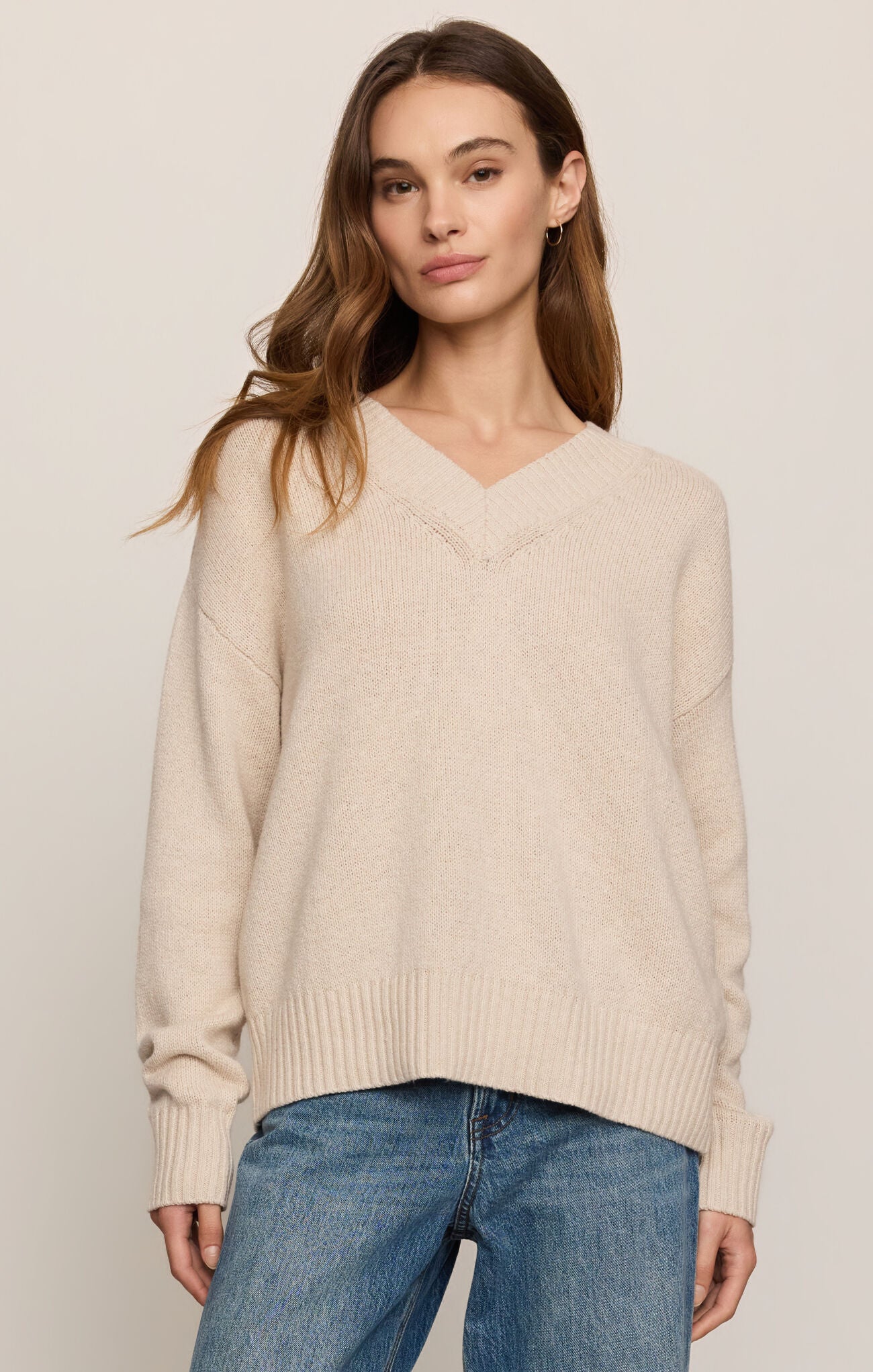 Woman wearing a beige sweater and blue jeans against a plain background