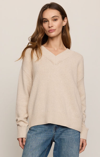 Woman wearing a beige sweater and blue jeans against a plain background