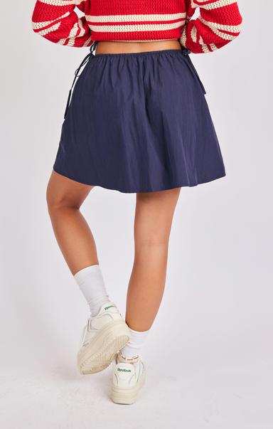 Person wearing a red and white striped sweater, navy skirt, and white sneakers on a light gray background
