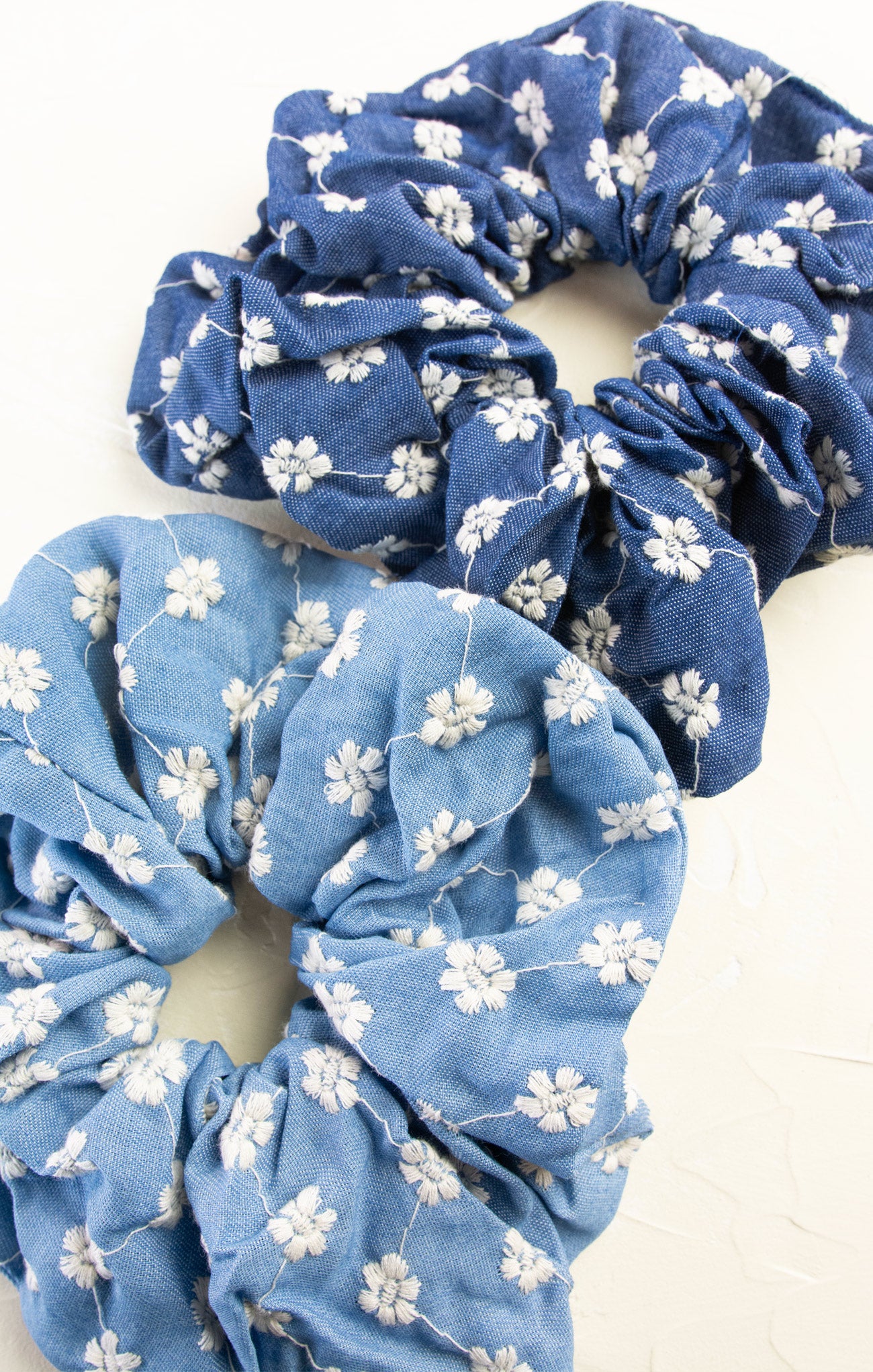 Two blue scrunchies with white floral patterns on a white background