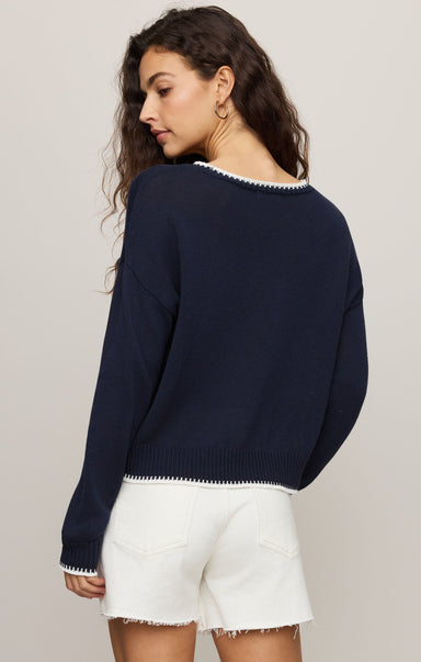 Woman wearing a navy sweater with white trim and white shorts on a plain background