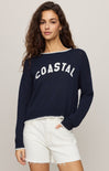 Woman wearing a navy sweater with 'COASTAL' text on a plain background
