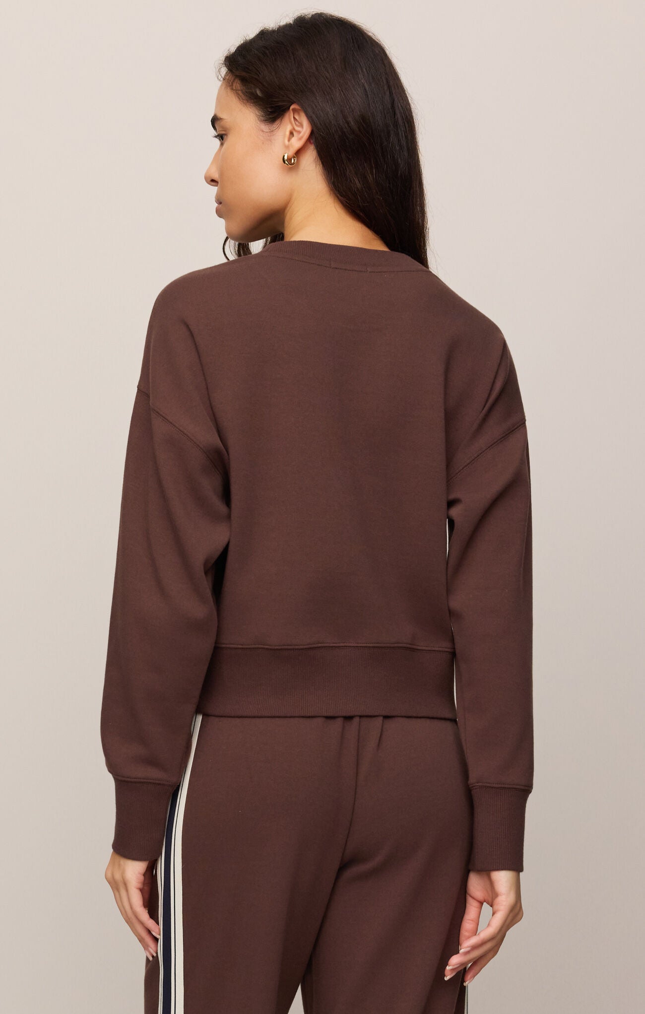 Woman wearing a brown sweatshirt and pants with white stripes on a beige background