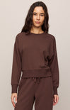 Woman wearing a brown sweatshirt and pants set against a plain background