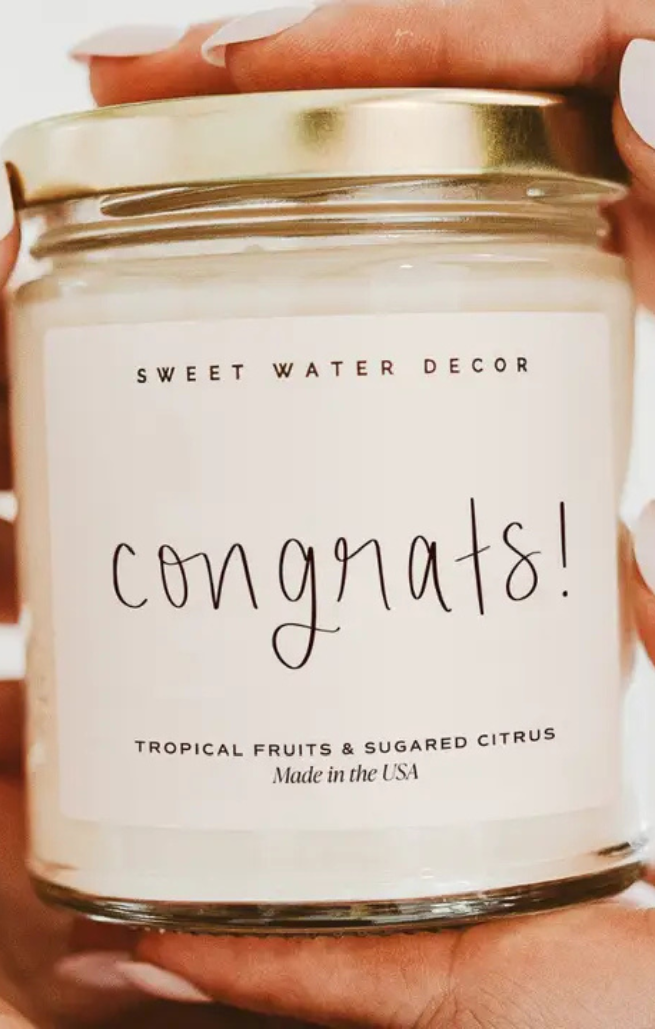 Candle with 'Sweet Water Decor' label and 'Congrats!' text held by a person.