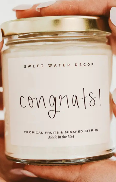 Candle with 'Sweet Water Decor' label and 'Congrats!' text held by a person.