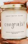 Candle with 'Sweet Water Decor' label and 'Congrats!' text held by a person.