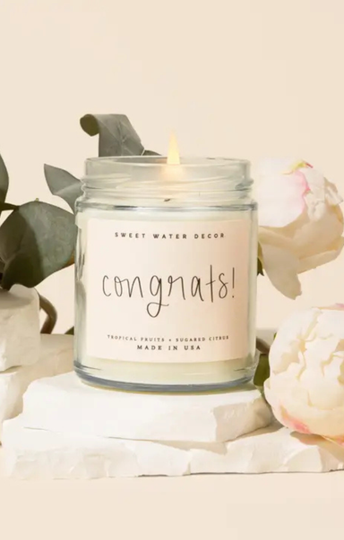 Candle in a jar labeled 'Congrats!' with floral and greenery in the background
