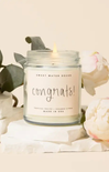 Candle in a jar labeled 'Congrats!' with floral and greenery in the background
