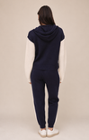 A woman shown from the back wearing a navy blue cropped hooded sweatshirt with contrasting off-white sleeves, matching navy jogger pants, and white sneakers, set against a plain beige studio background.