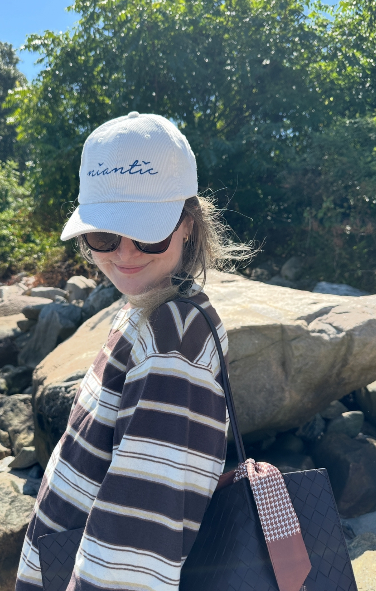 Person wearing a white cap with 'Niantic' logo, sunglasses, and striped shirt outdoors.