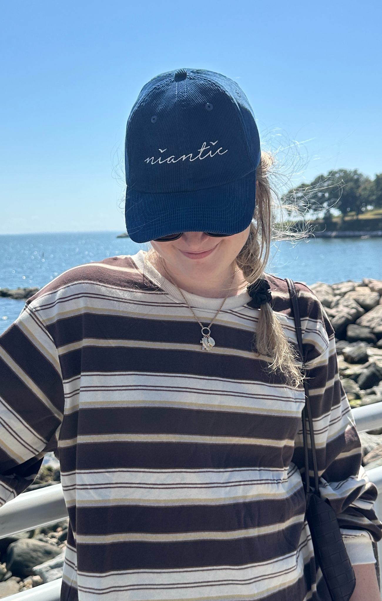 Person wearing a blue cap with 'niantic' on it by the ocean.