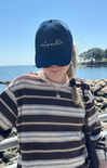 Person wearing a blue cap with 'niantic' on it by the ocean.