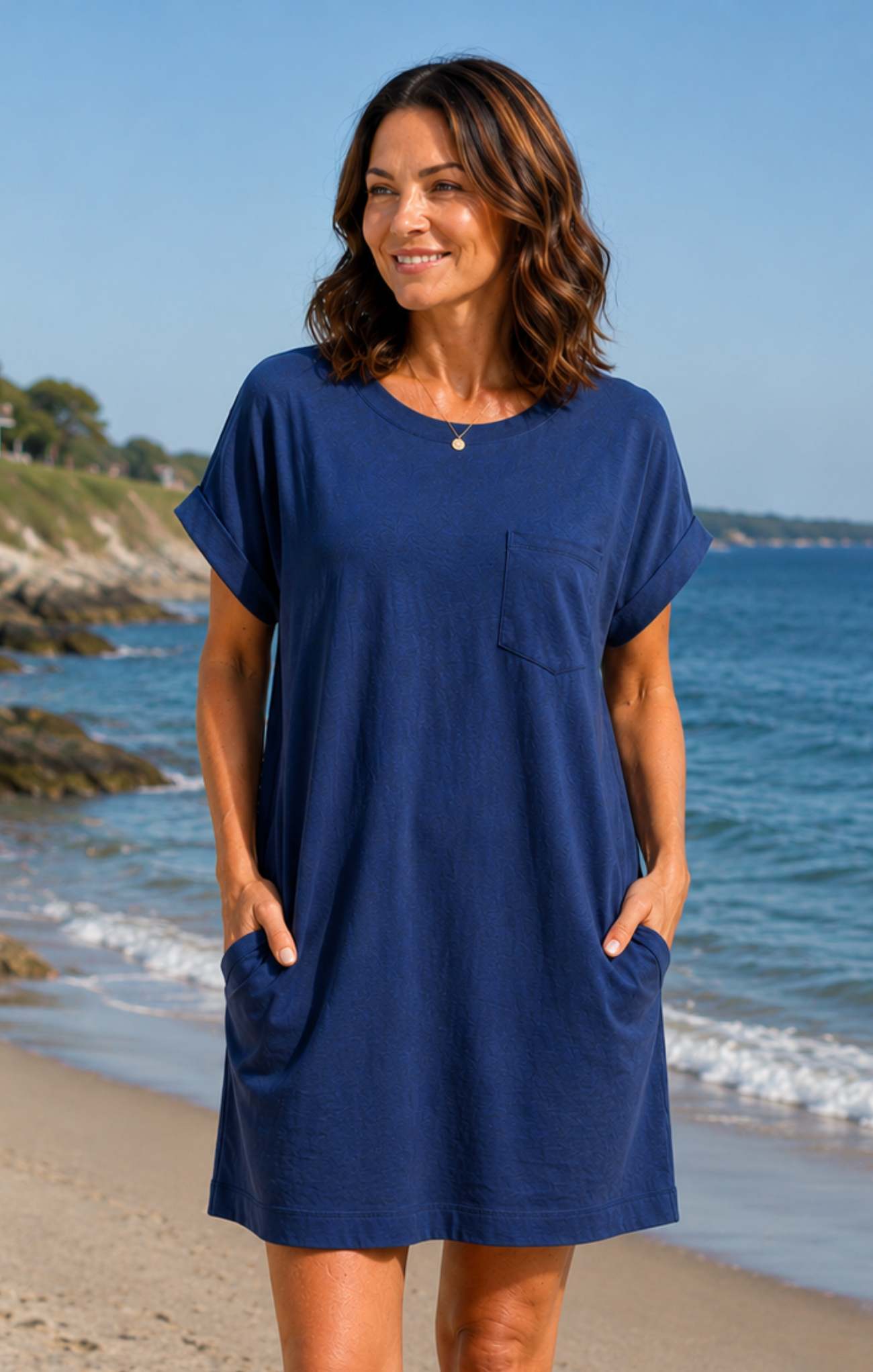 Woman wearing a blue dress standing on a beach with ocean and sky in the background