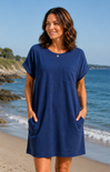 Woman wearing a blue dress standing on a beach with ocean and sky in the background