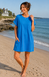 Woman in a blue dress standing on a beach with ocean and house in the background