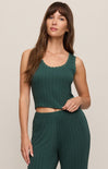 Woman wearing a green sleeveless top and pants against a beige background