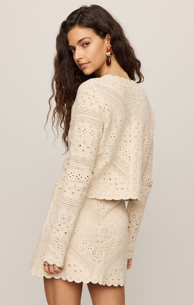 Woman wearing a beige crochet dress against a plain background