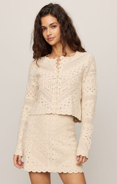 Woman wearing a cream-colored crochet outfit against a plain background