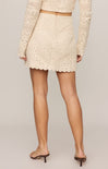 Person wearing a beige crochet skirt and top on a plain background