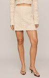 Person wearing a beige crochet skirt and top on a plain background