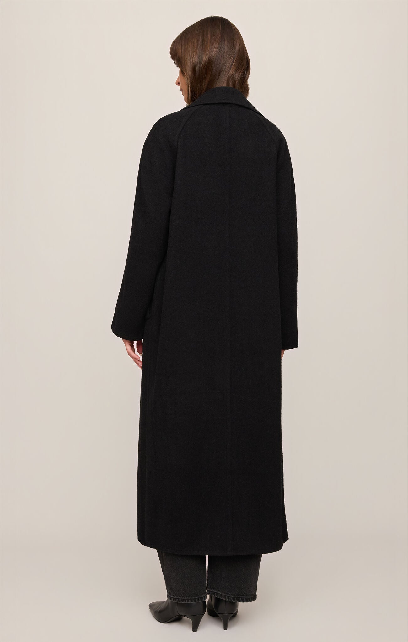 Person wearing a long black coat on a plain background