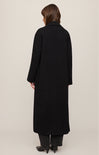 Person wearing a long black coat on a plain background