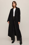 Woman wearing a long black coat on a plain background