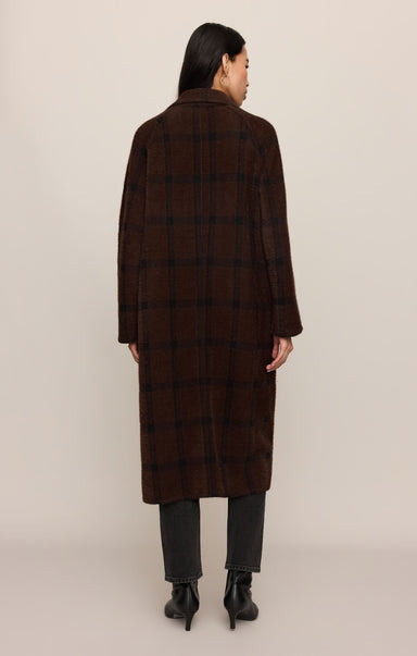 Person wearing a brown checkered coat on a beige background