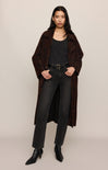 Woman wearing a brown coat, black top, and jeans on a beige background