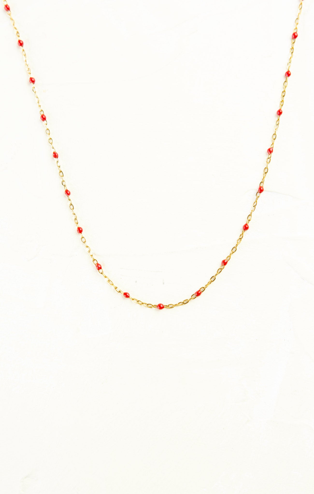 Necklace with red beads on a gold chain against a white background