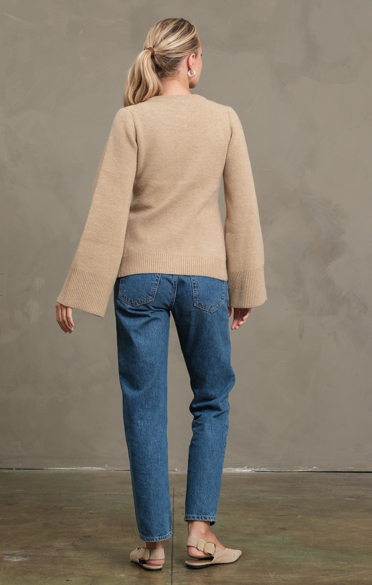 Woman wearing a beige sweater and blue jeans against a plain background