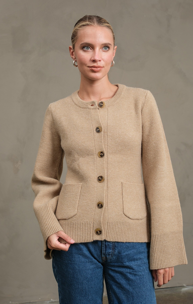 Woman wearing a beige cardigan with brown buttons against a plain background