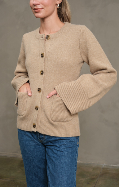 Woman wearing a beige cardigan with button details against a plain background
