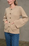 Woman wearing a beige cardigan with button details against a plain background