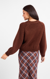 Woman wearing a brown knitted sweater and plaid skirt on a white background