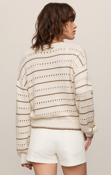 Woman wearing a striped sweater and white shorts against a plain background
