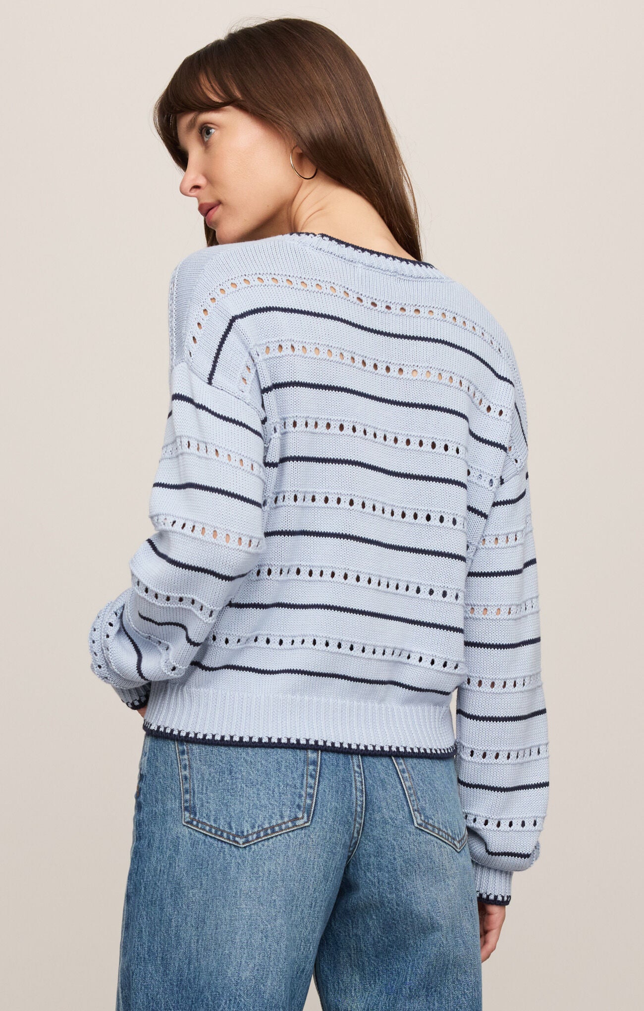 Woman wearing a light blue striped sweater with decorative elements on a beige background
