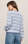Woman wearing a light blue striped sweater with decorative elements on a beige background