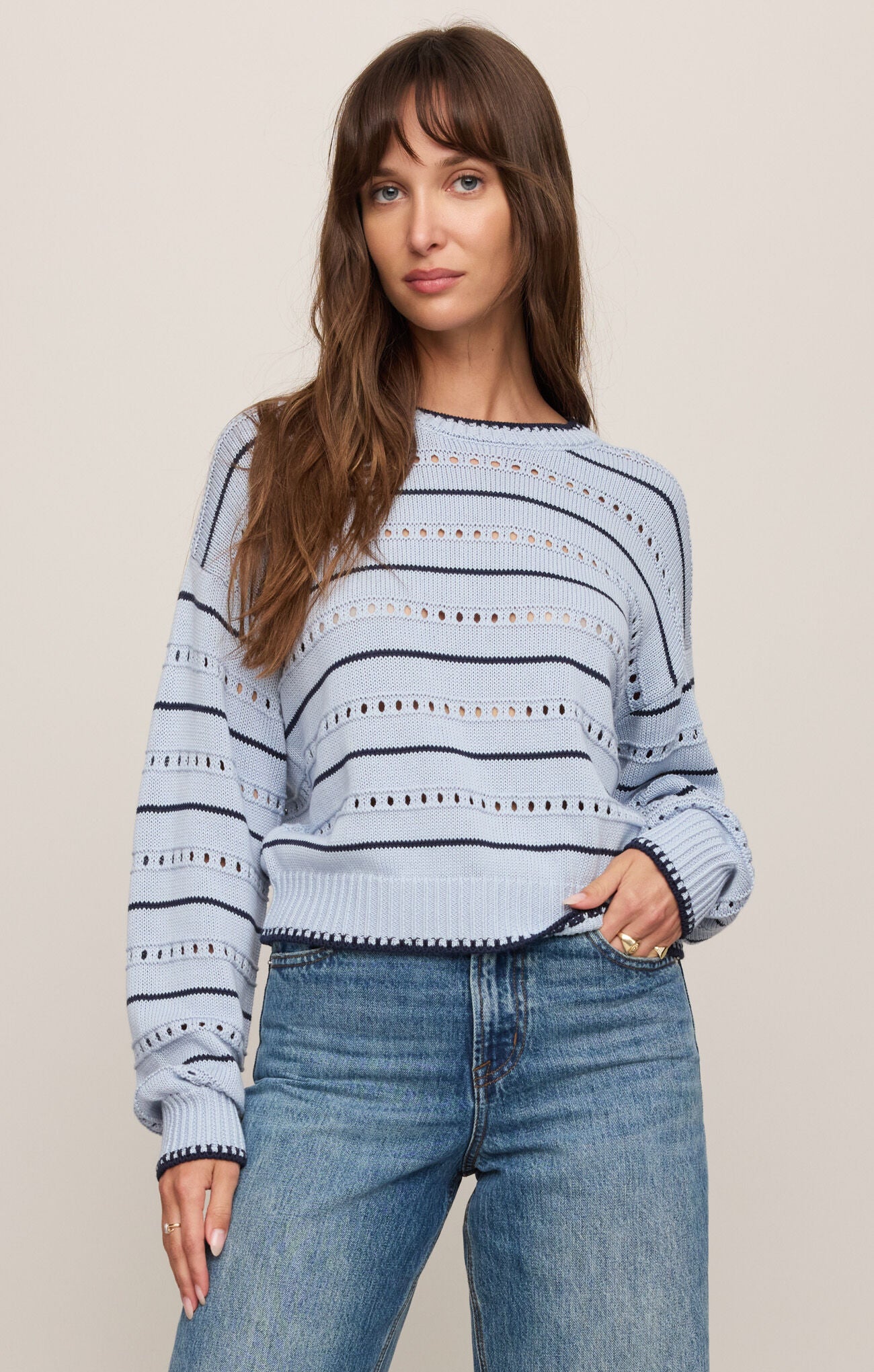 Woman wearing a blue and white striped sweater and jeans on a beige background