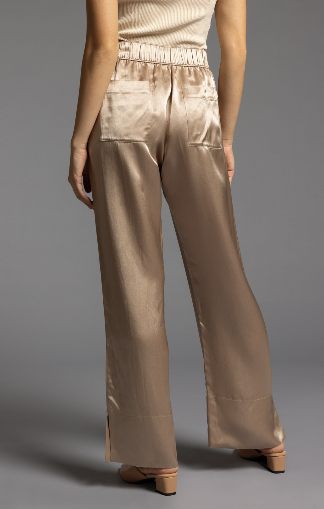 Beige satin pants worn by a person on a gray background
