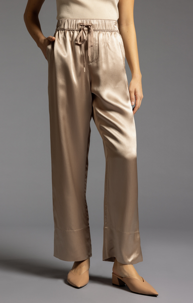 Beige satin pants worn by a person on a gray background