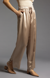 Beige satin pants worn by a person on a gray background
