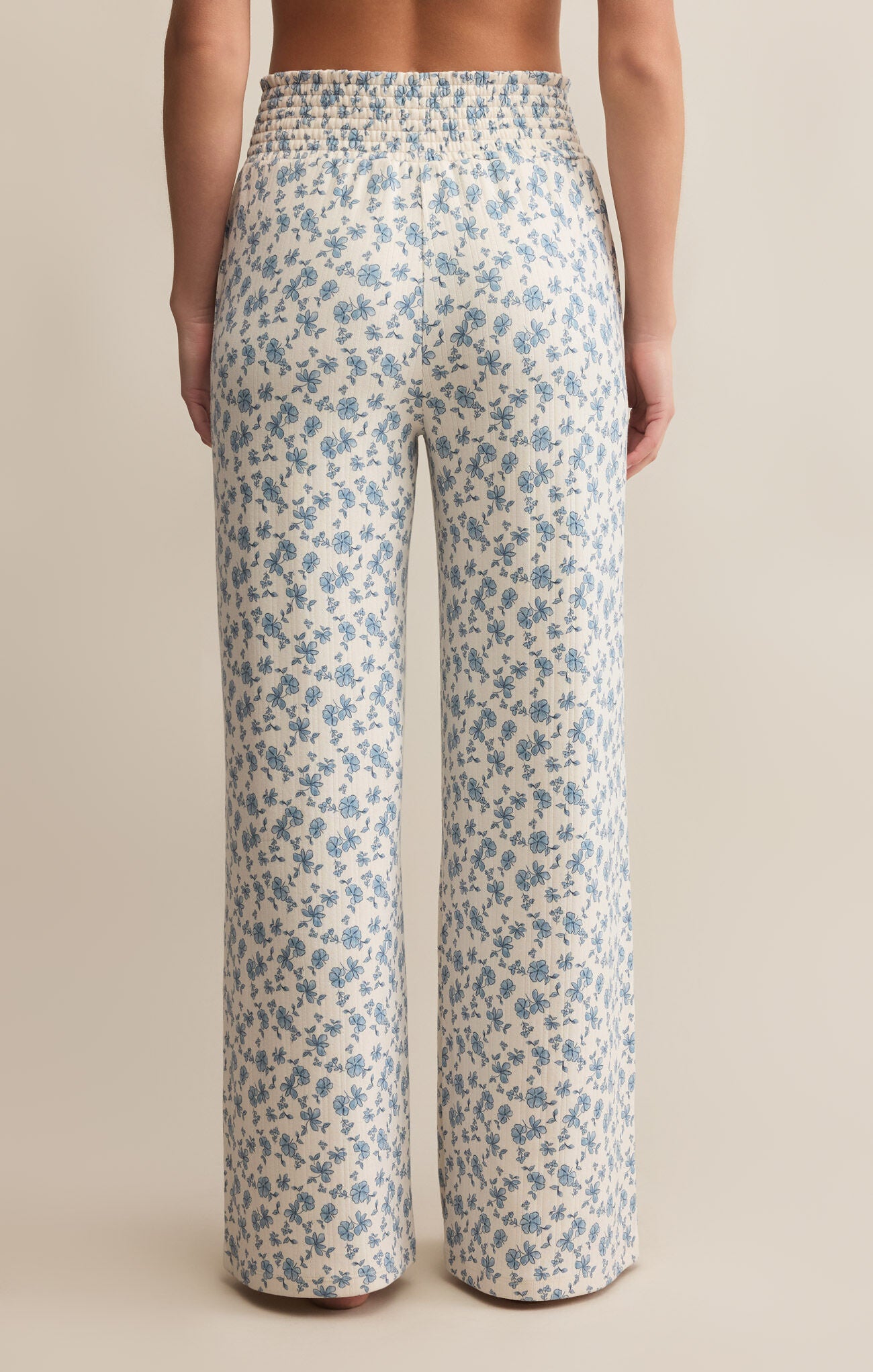 A pair of high-waisted, full-length pants with a smocked waistband and a blue floral pattern on a white background.