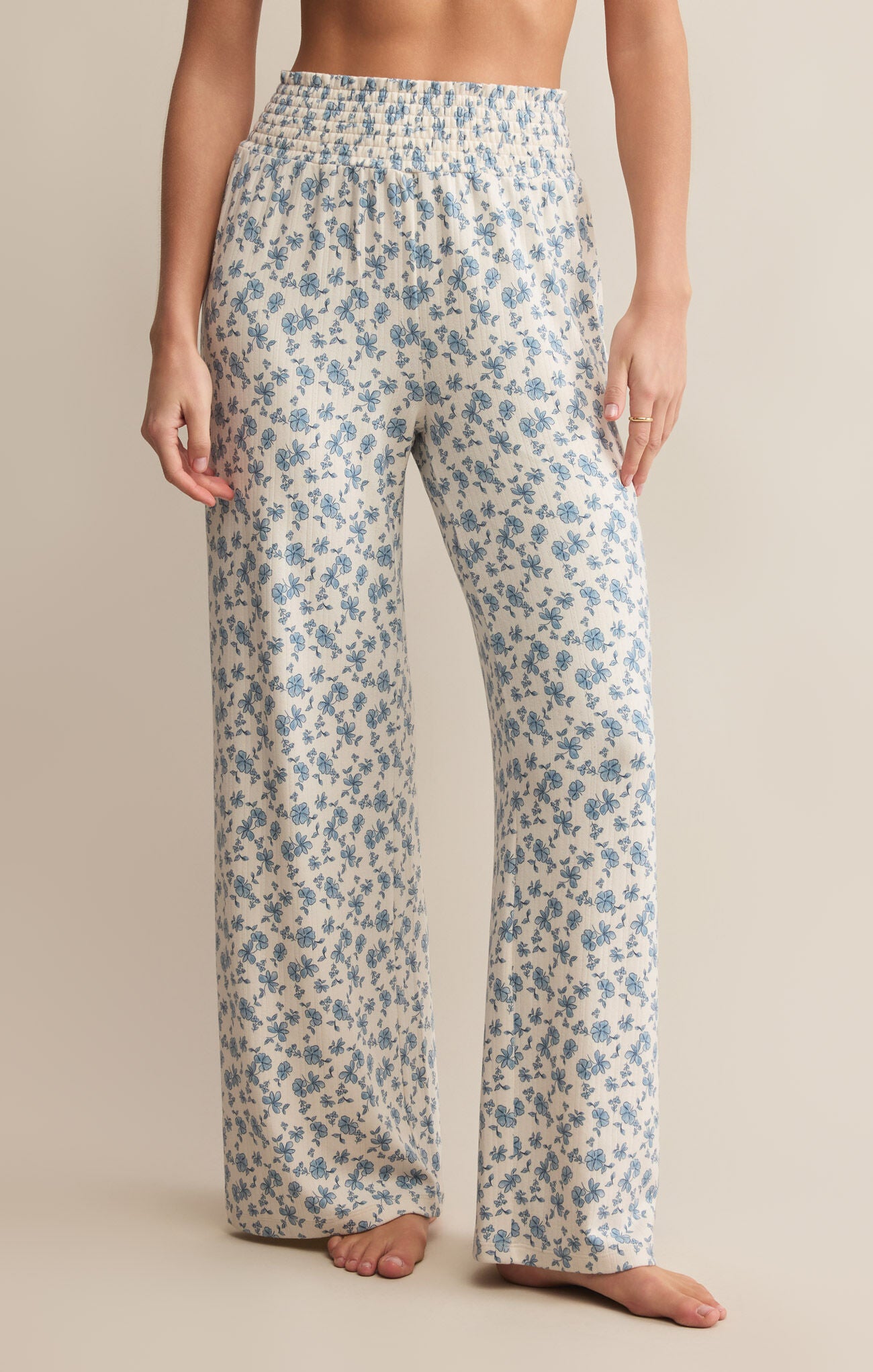A pair of high-waisted, full-length pants with a smocked waistband and a blue floral pattern on a white background.