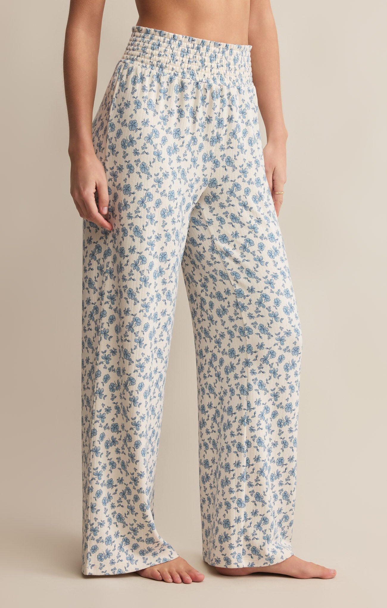 A pair of high-waisted, full-length pants with a smocked waistband and a blue floral pattern on a white background.